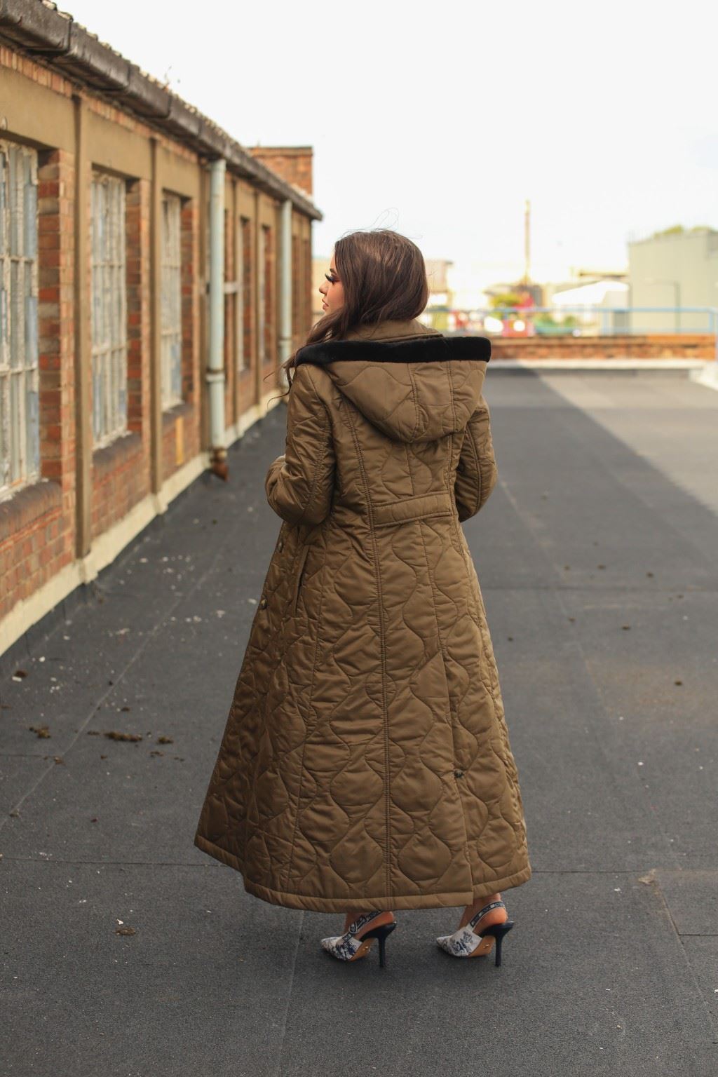 Person wearing a long quilted coat on a rooftop with a building in the background