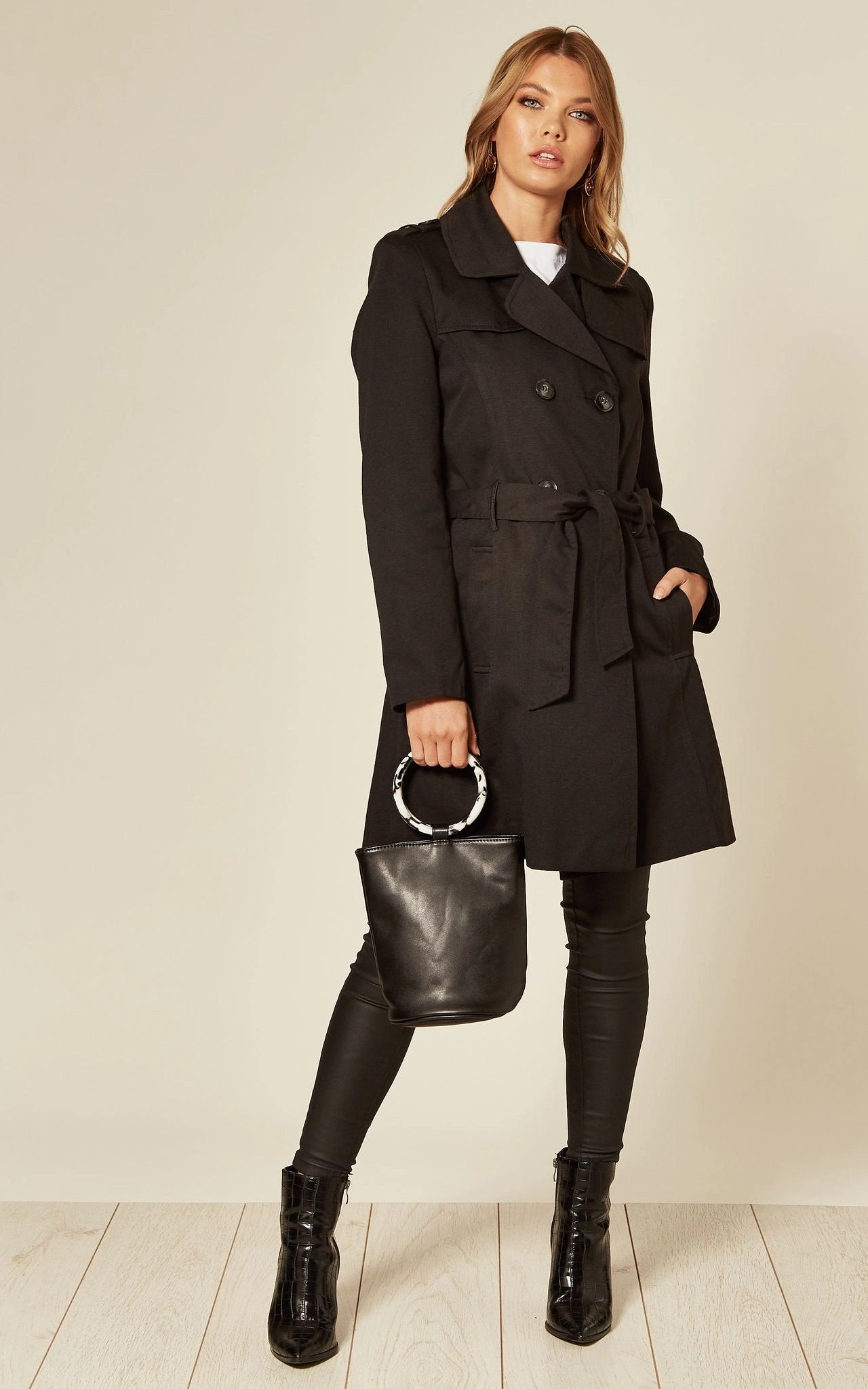 Woman wearing a black coat, holding a black handbag, on a plain background