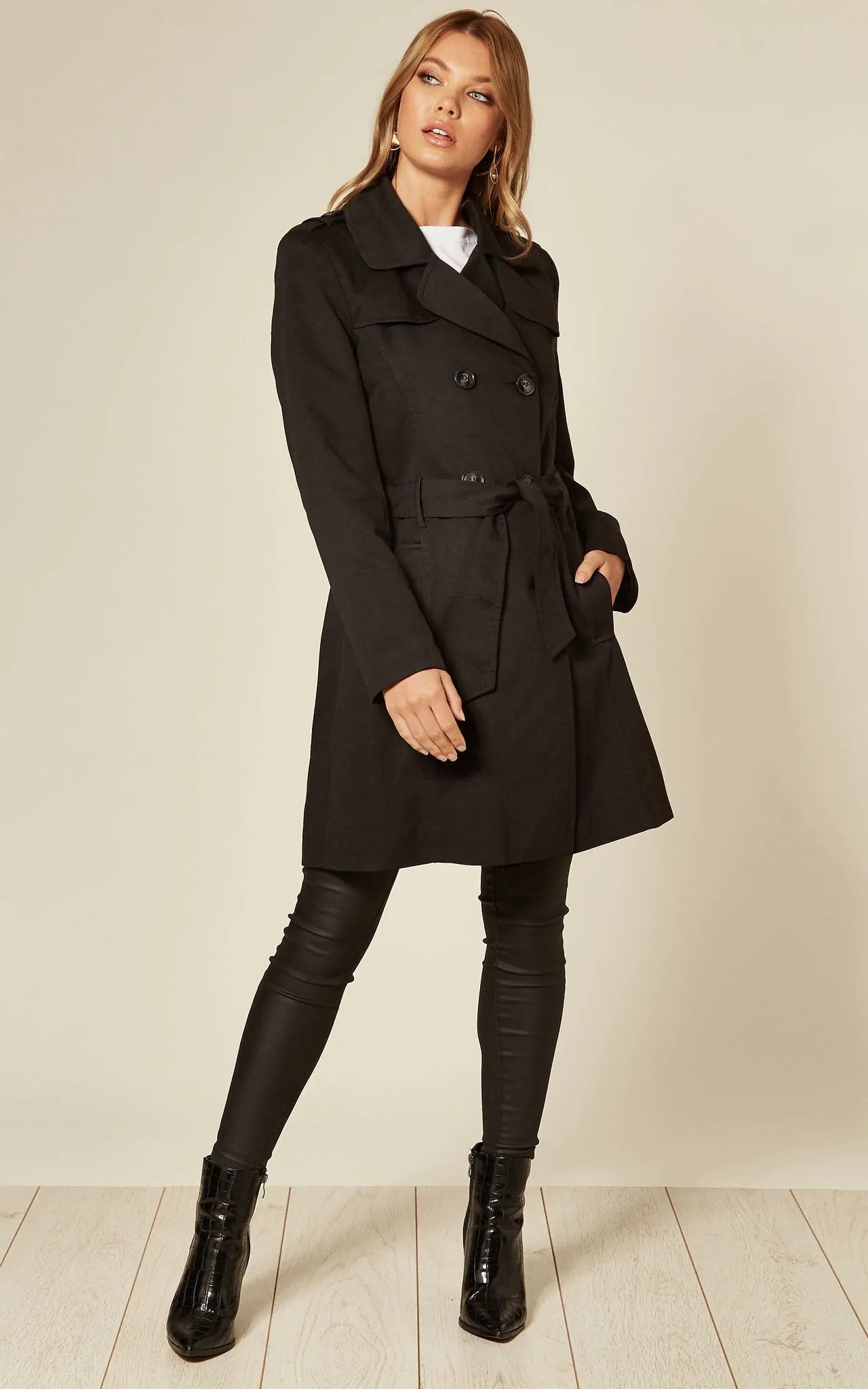 Woman wearing a black coat with a belt on a plain background