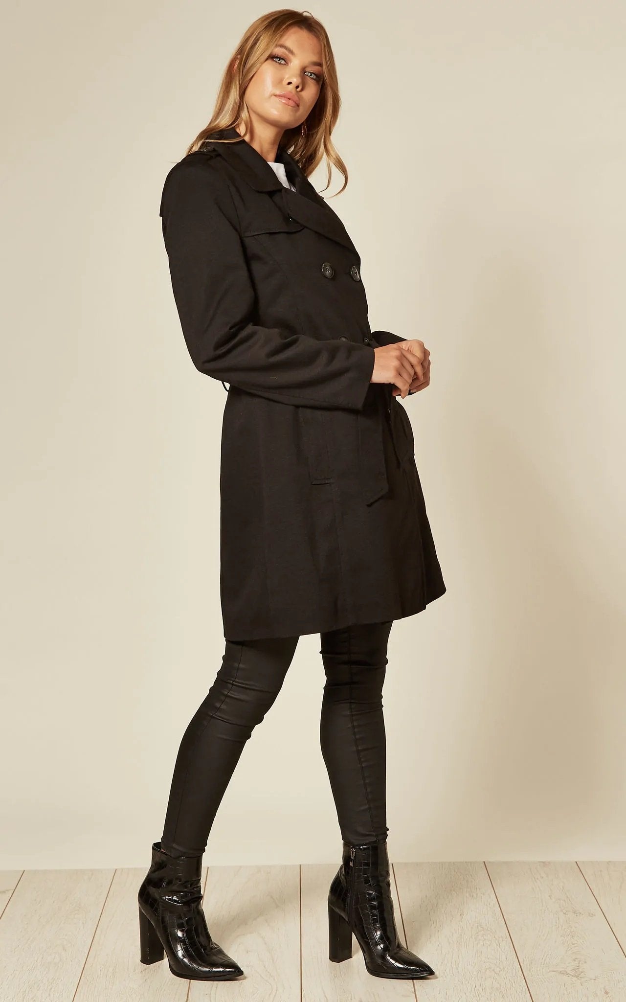 Woman wearing a black trench coat and black boots on a plain background