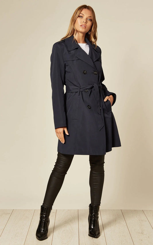 Woman wearing a navy trench coat with a plain background