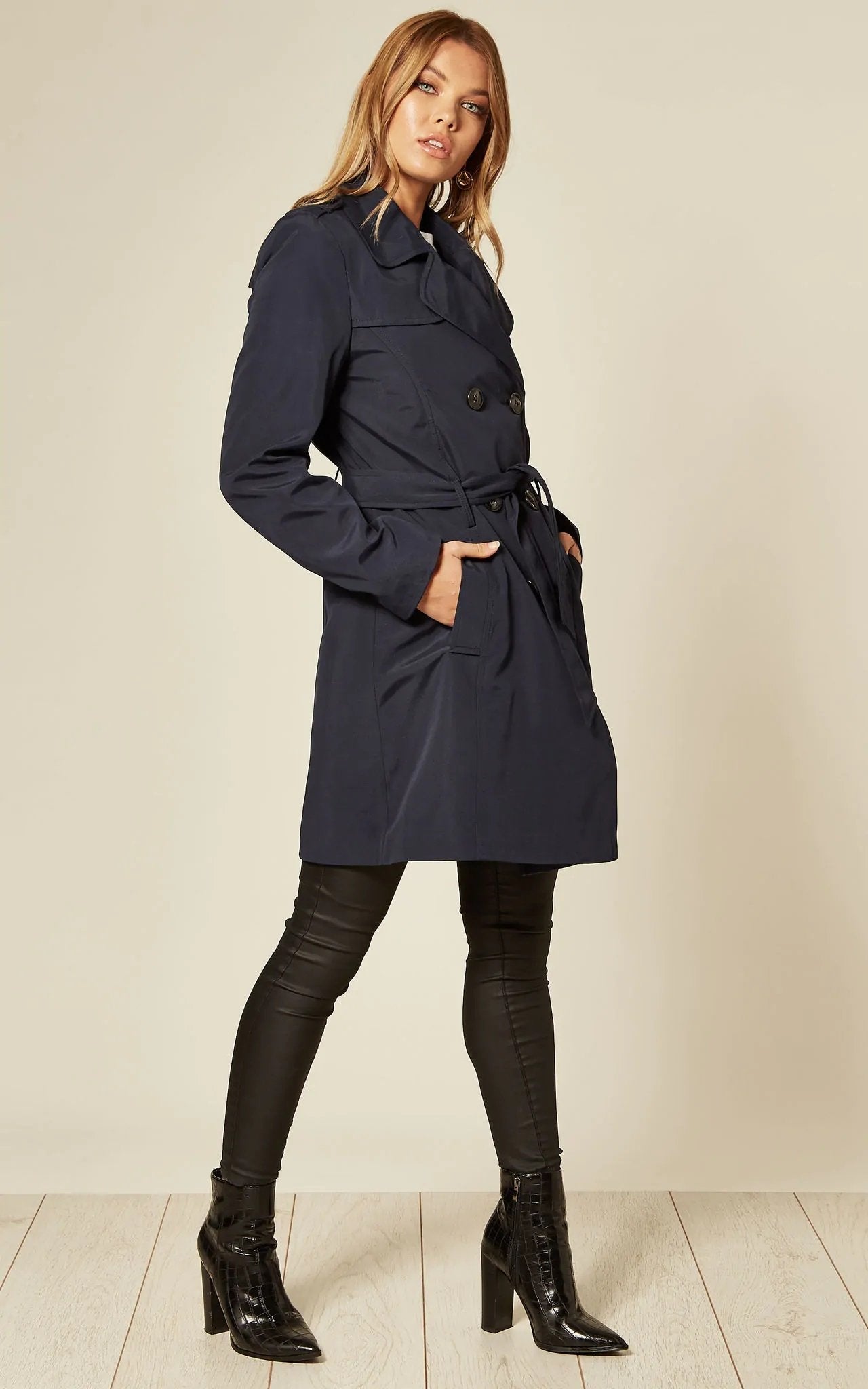Woman wearing a navy trench coat with a plain background