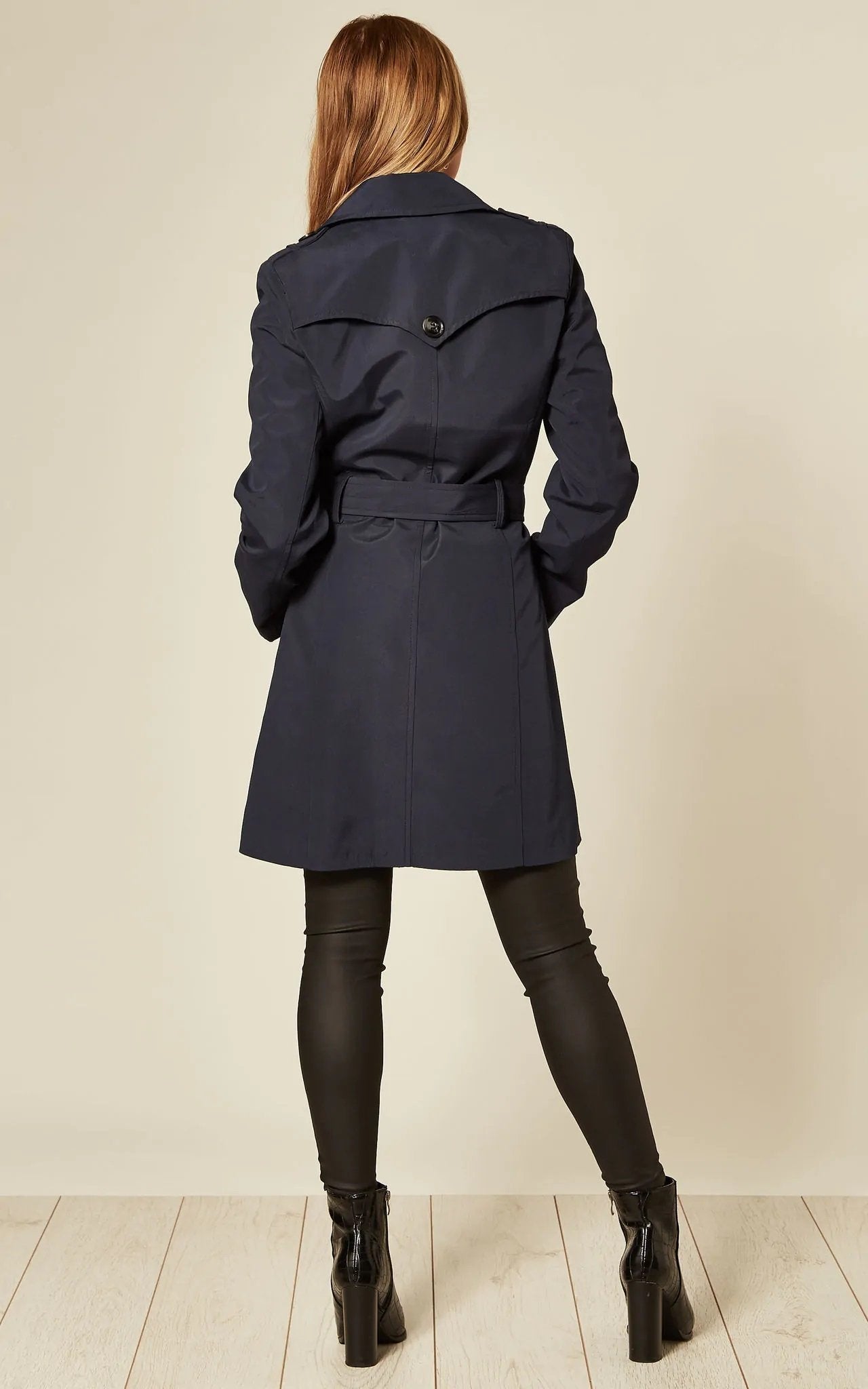 Person wearing a navy trench coat on a plain background