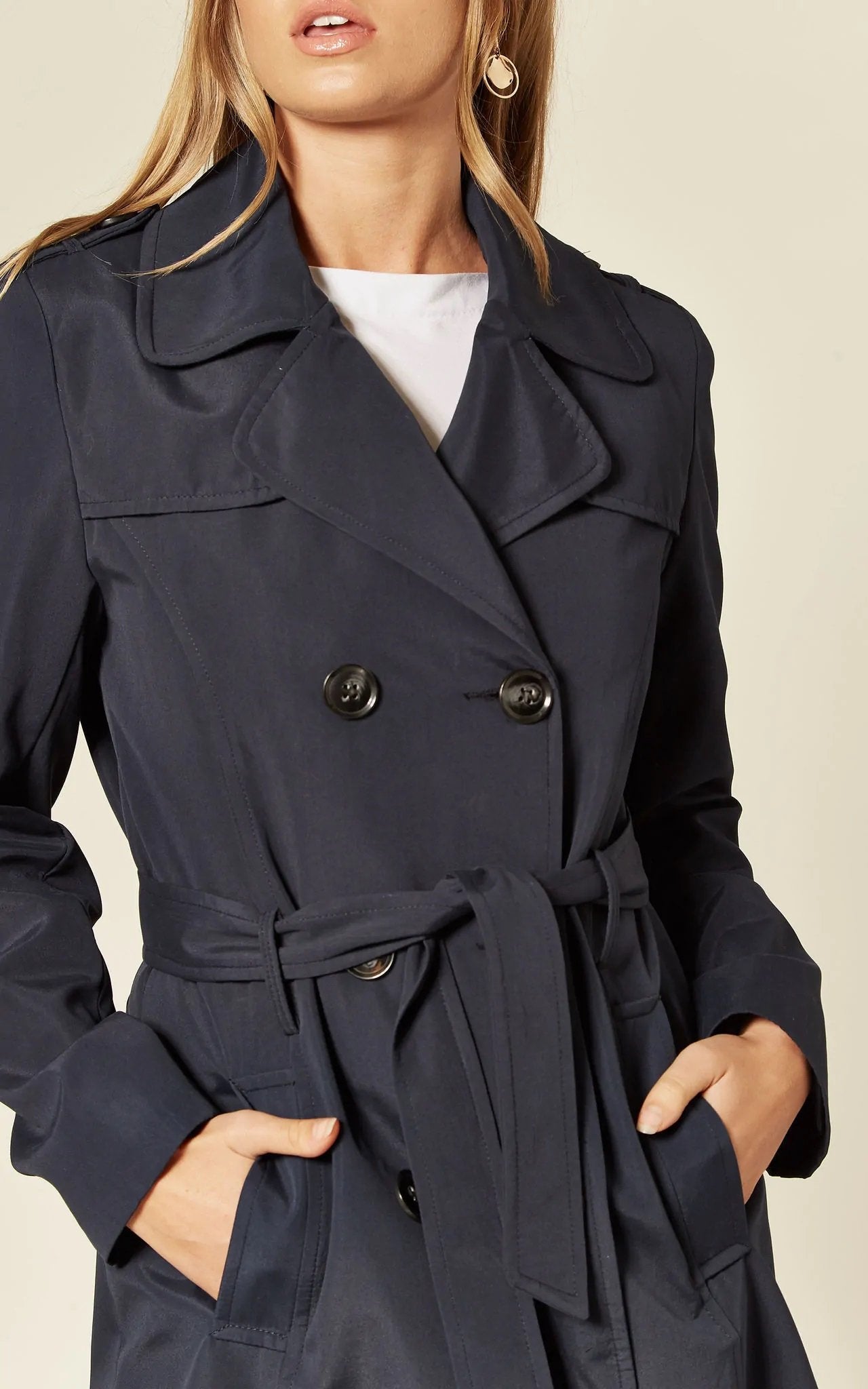 Navy trench coat worn by a model on a beige background