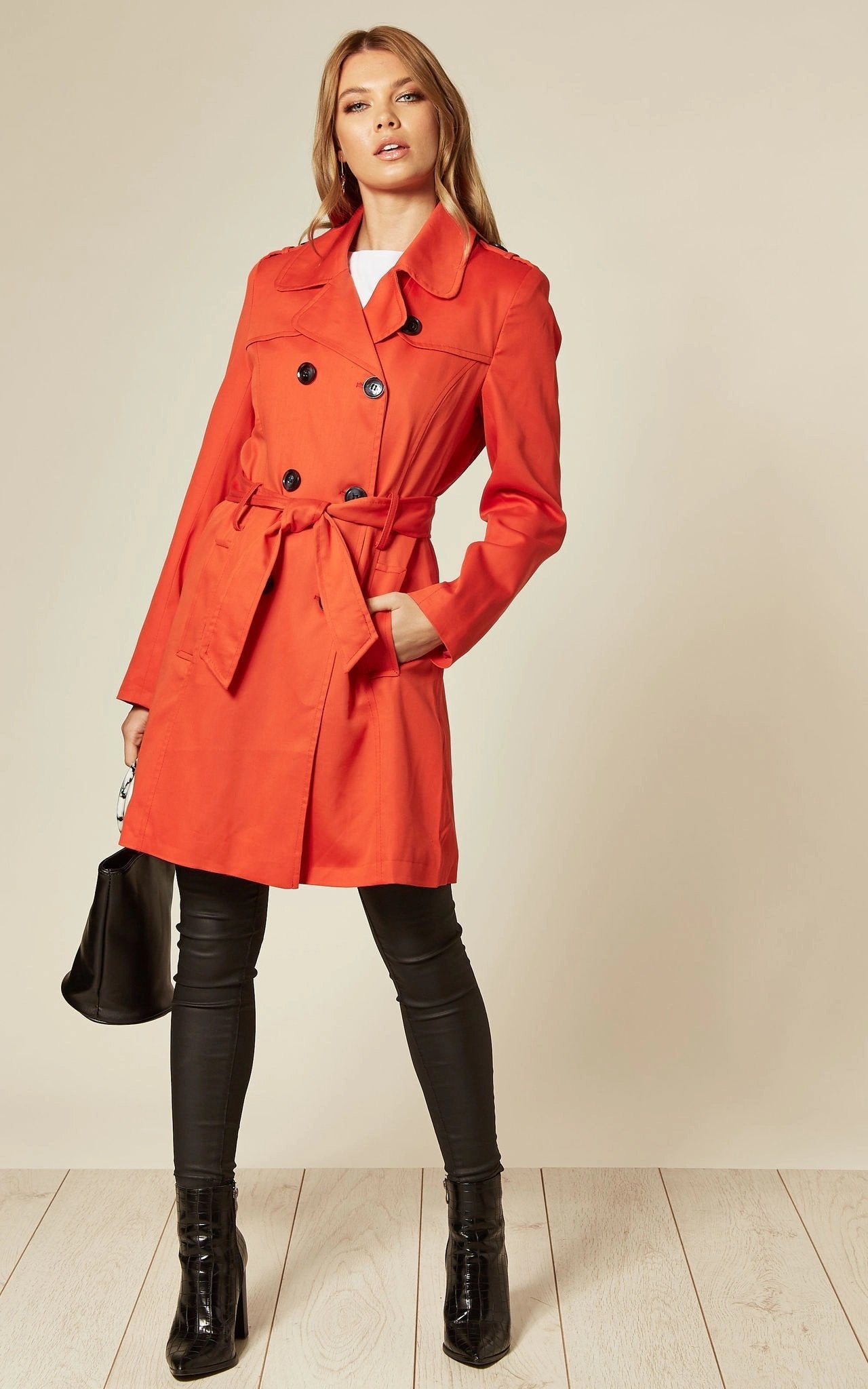 Woman wearing a bright red trench coat against a plain background