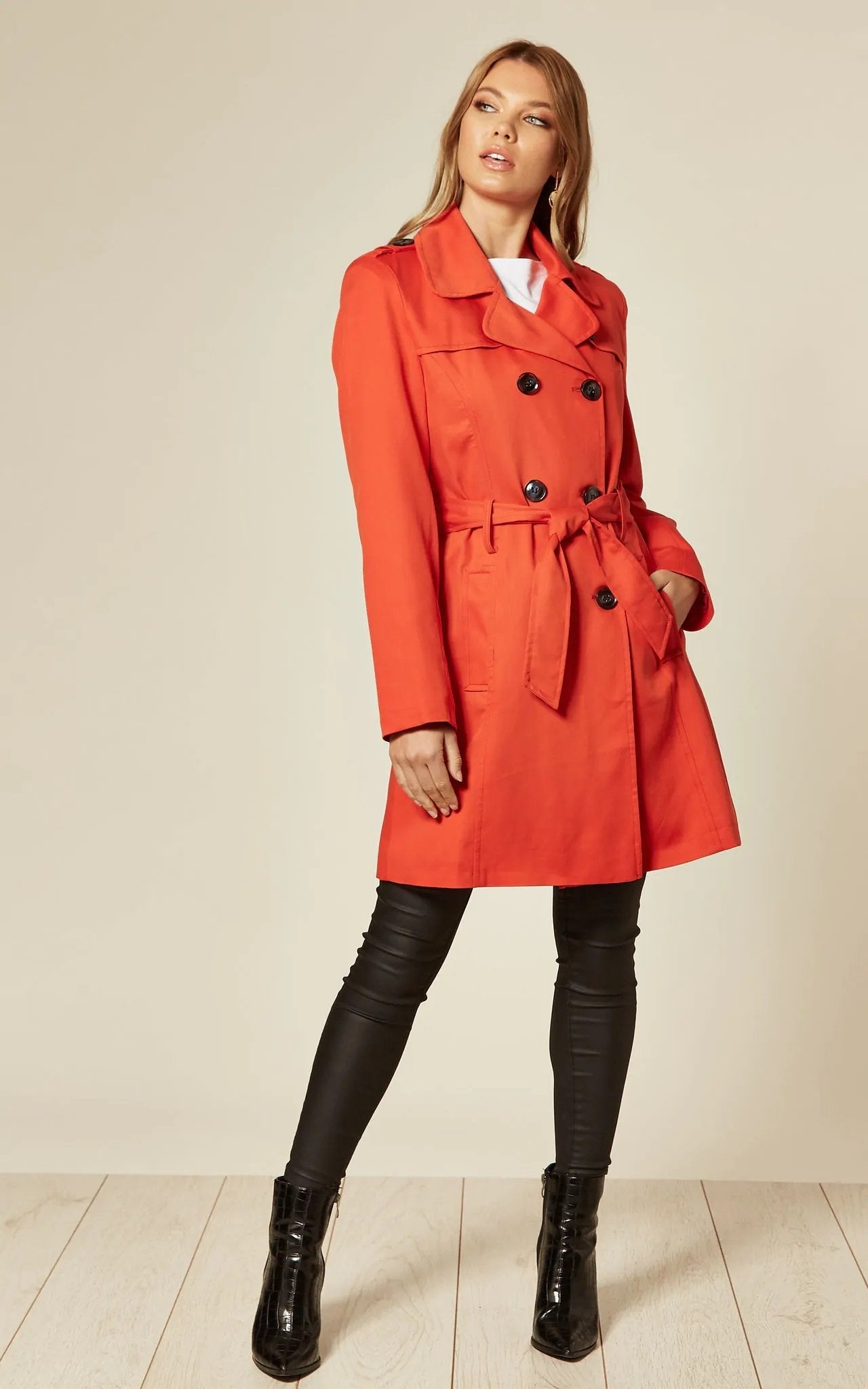 Woman wearing an orange trench coat with black buttons on a beige background