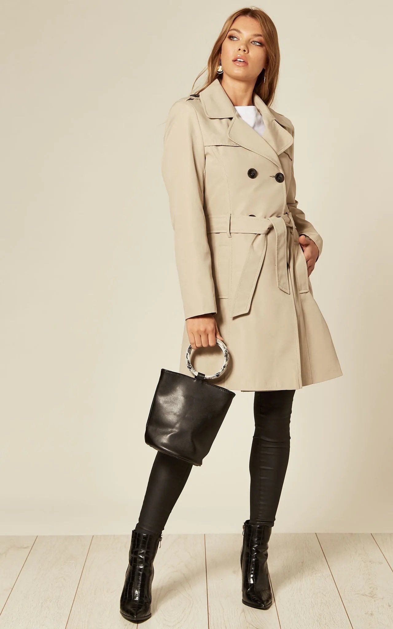 Woman wearing a beige trench coat holding a black handbag on a white background