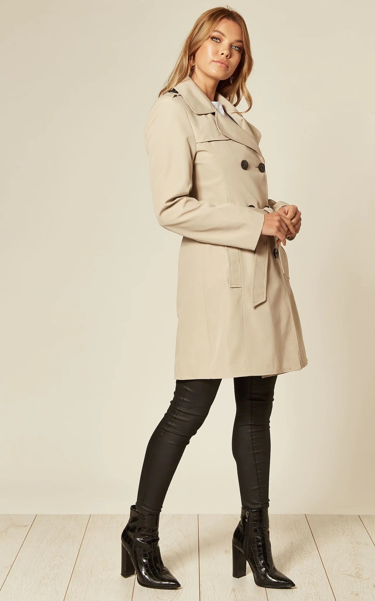Woman wearing a beige trench coat with black leather pants and boots on a white background