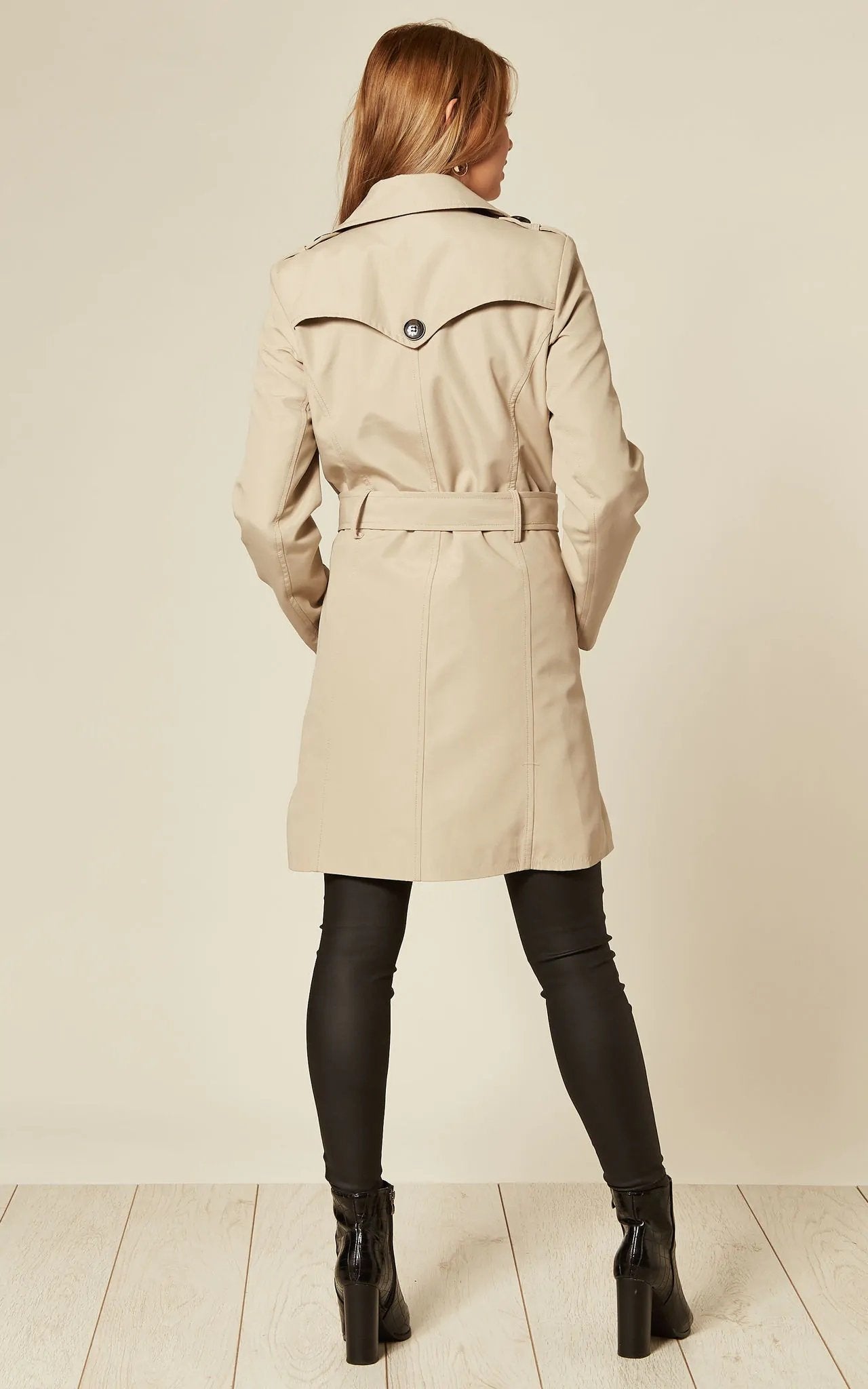 Woman wearing a beige trench coat on a plain background