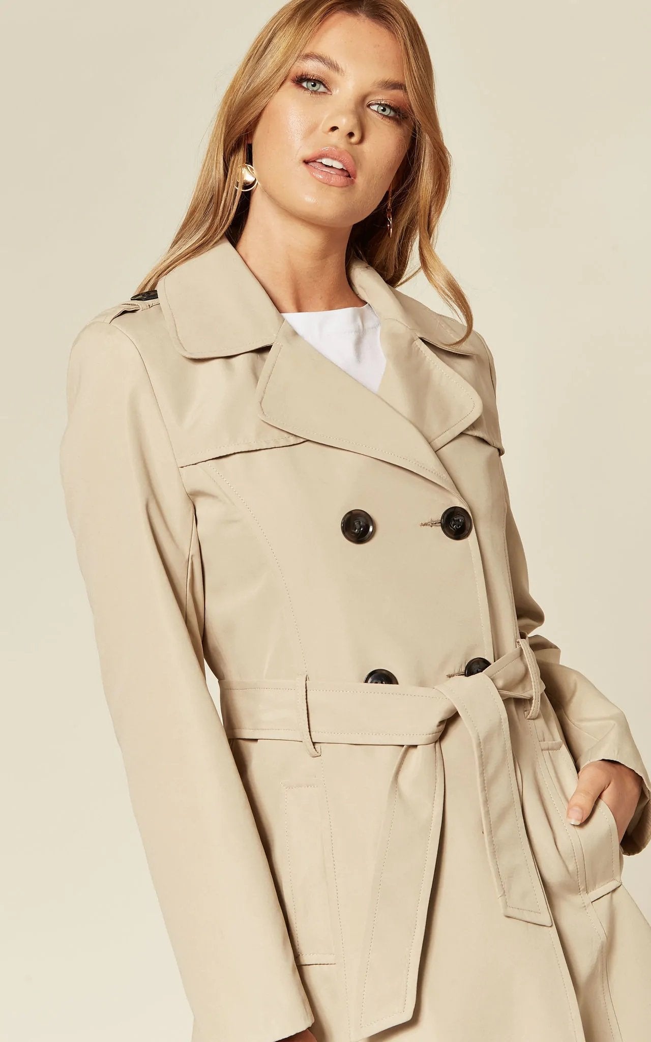 Woman wearing a beige trench coat against a plain background