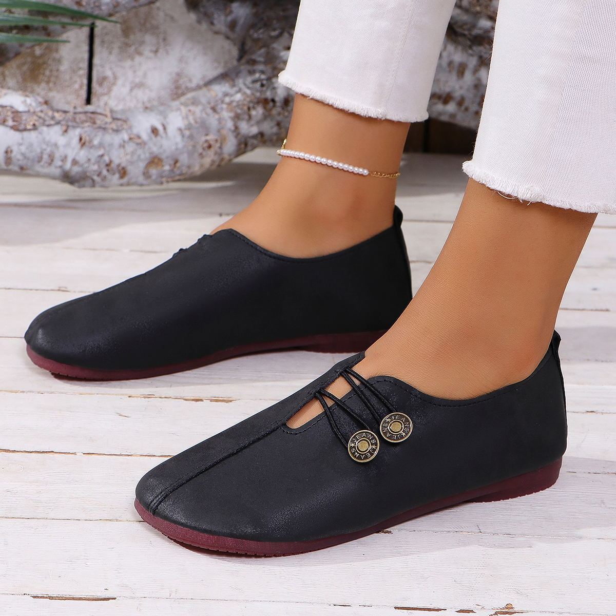 Black loafers with gold buttons worn by a person on a wooden floor.
