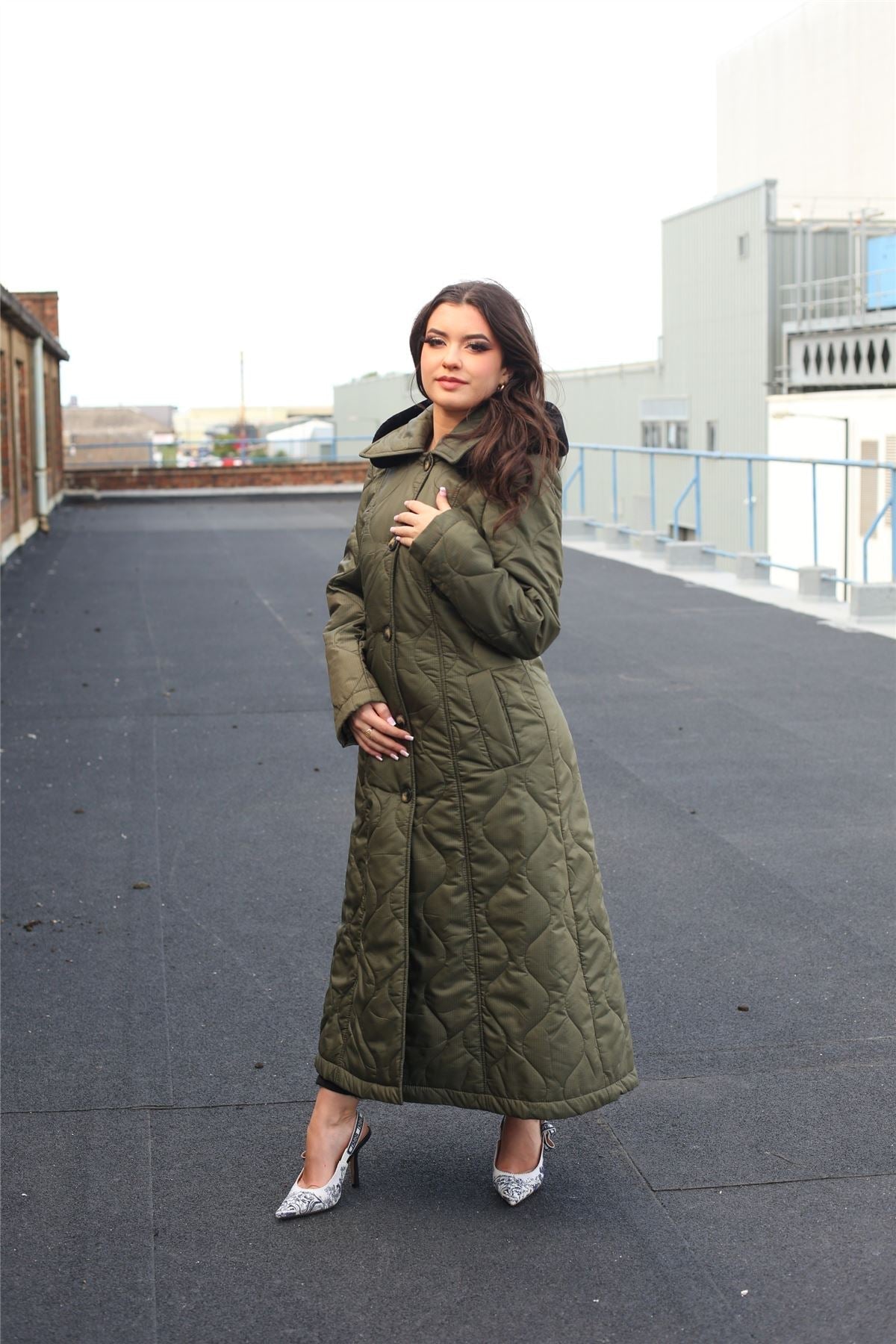 Woman wearing a long green quilted coat on a rooftop.
