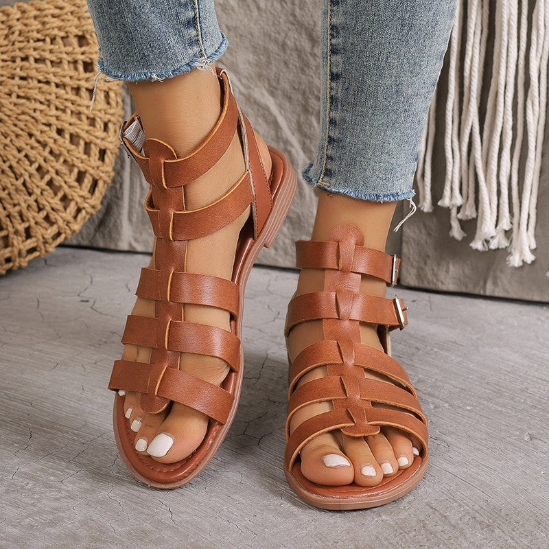 Brown strappy sandals worn with light blue jeans on a wooden floor.
