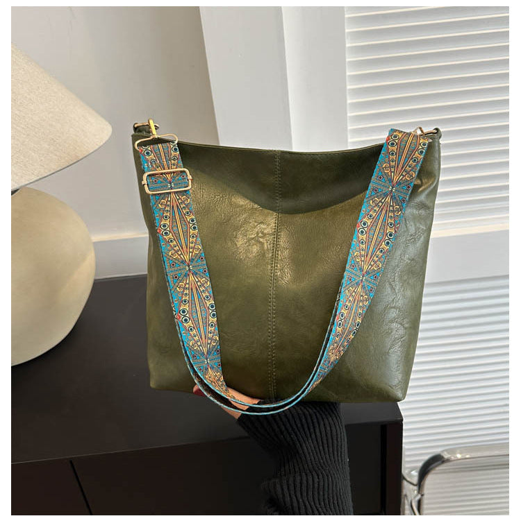 Green leather handbag with decorative strap on a dark surface