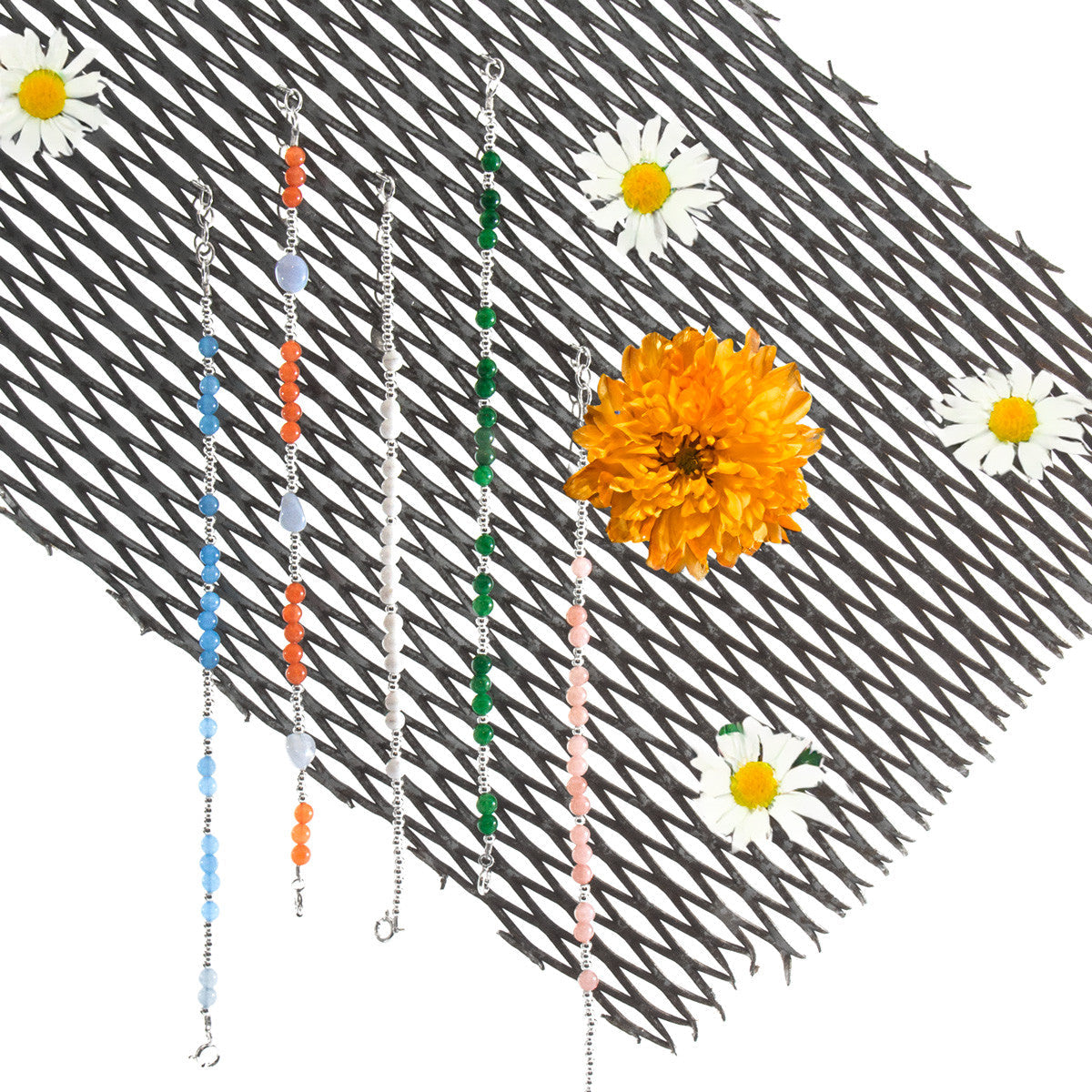 Three beaded chains with colorful beads on a textured surface with flowers.