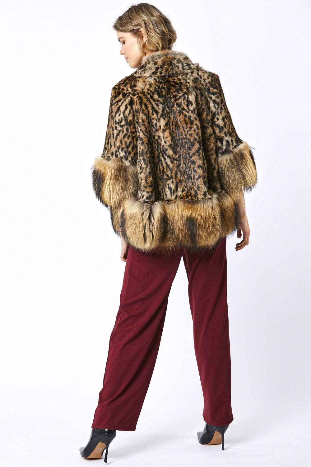 Woman wearing a leopard print fur coat and burgundy pants on a white background