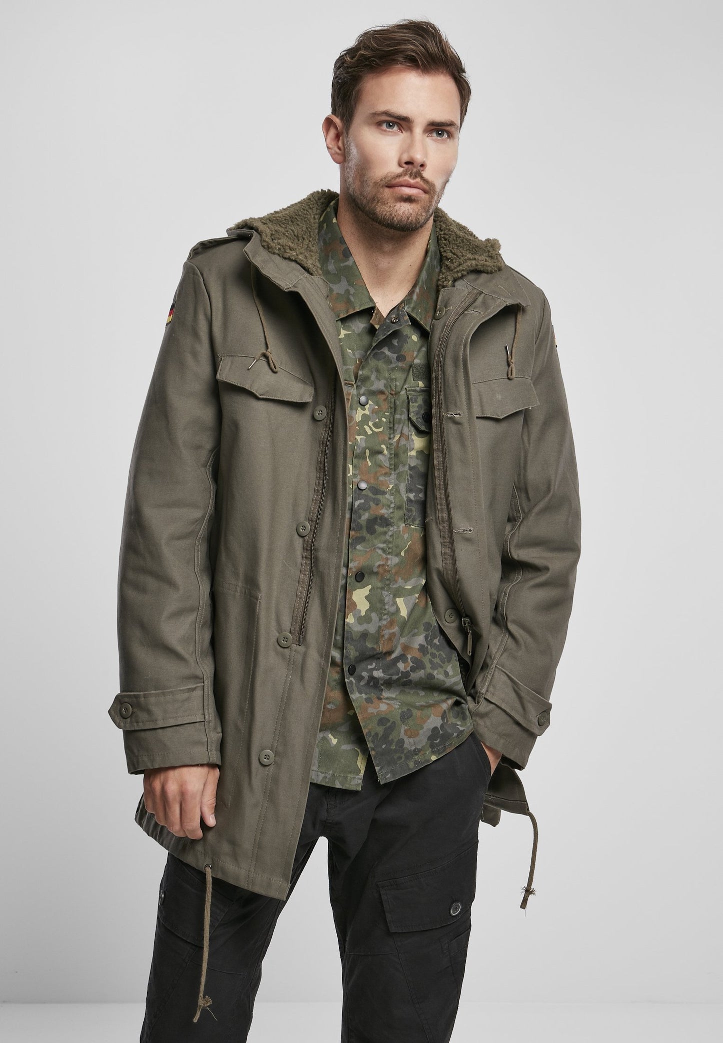 Man wearing a green hooded jacket over a camouflage shirt on a white background