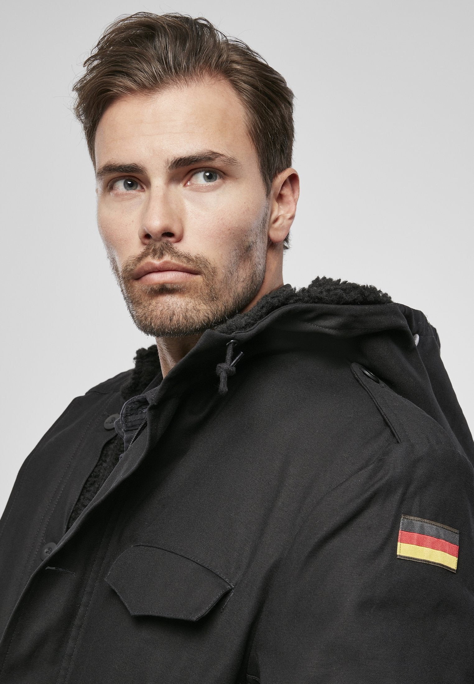 Man wearing a black coat with a flag patch on a gray background