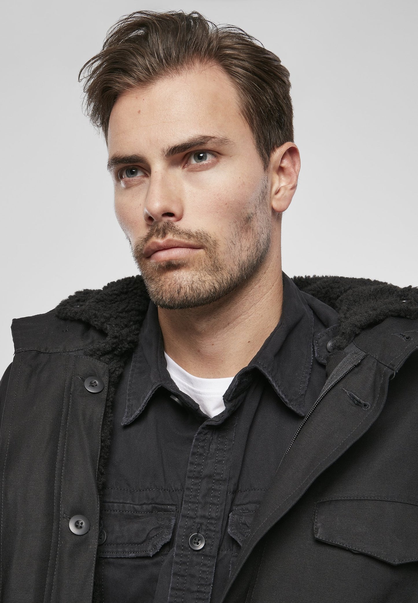 Man wearing a black coat with a fur-lined hood against a plain background