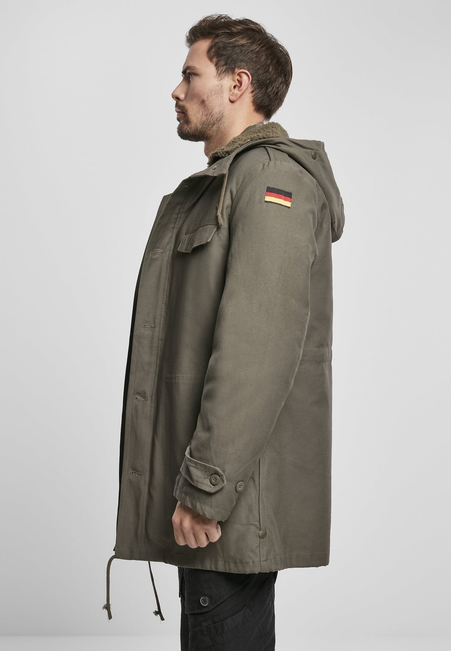 Man wearing a green parka with a German flag patch on a white background