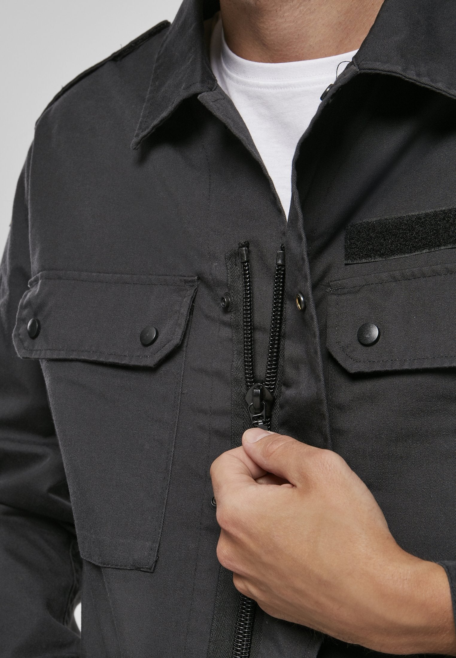 Person wearing a dark jacket with a hand zipping it up, on a light gray background