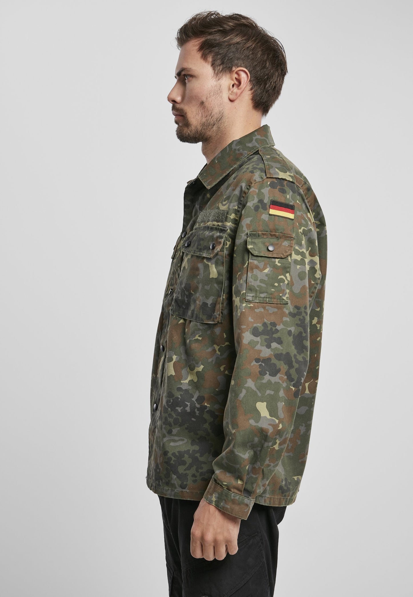 Man wearing a camouflage military jacket with a flag patch on a light gray background