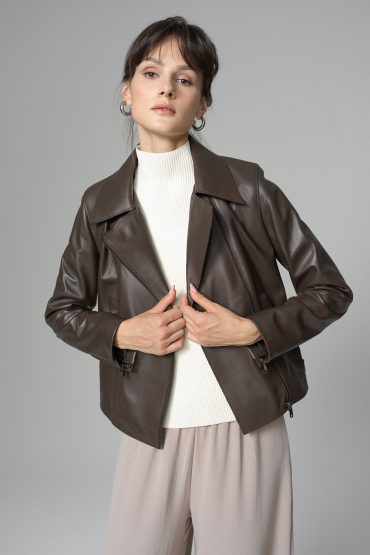 Woman wearing a brown leather jacket over a white top and beige pants on a gray background