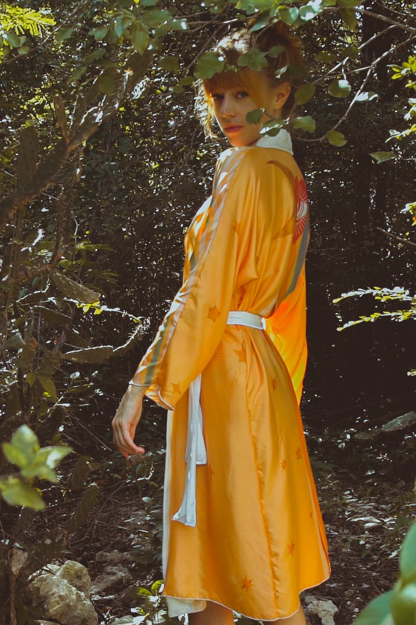 Person wearing a bright yellow dress with a white belt standing in a forest setting.