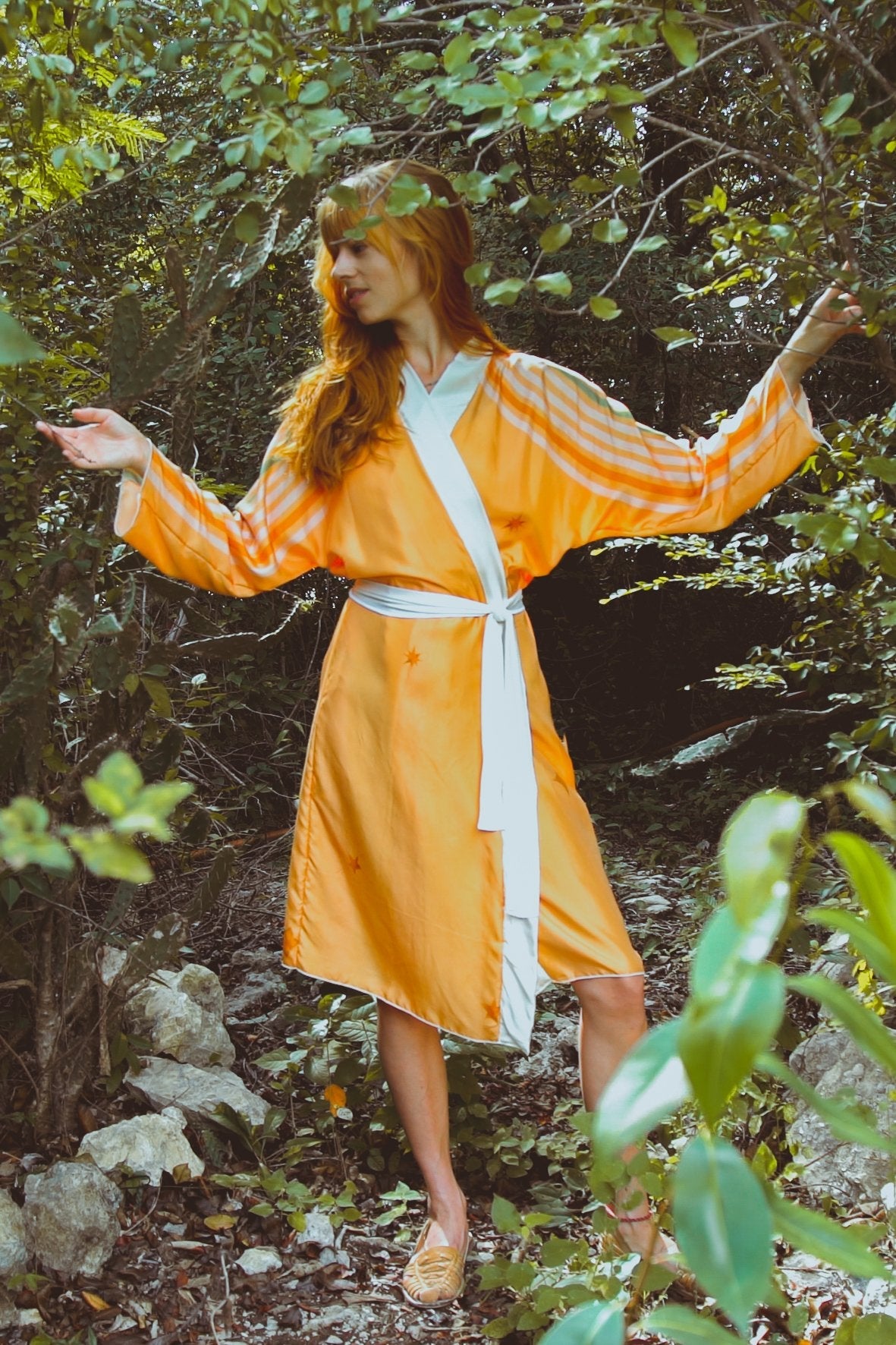 Woman in an orange dress with a white belt standing in a forest setting