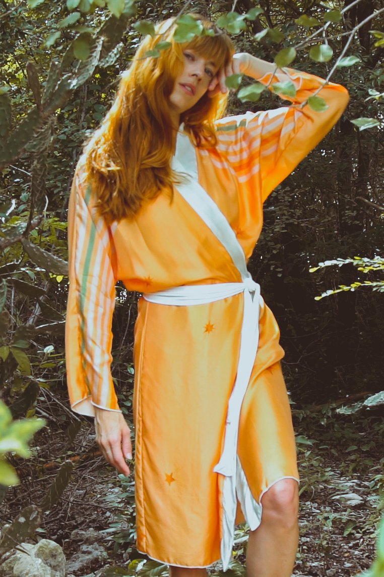 Woman in an orange dress with a white belt standing in a forest setting