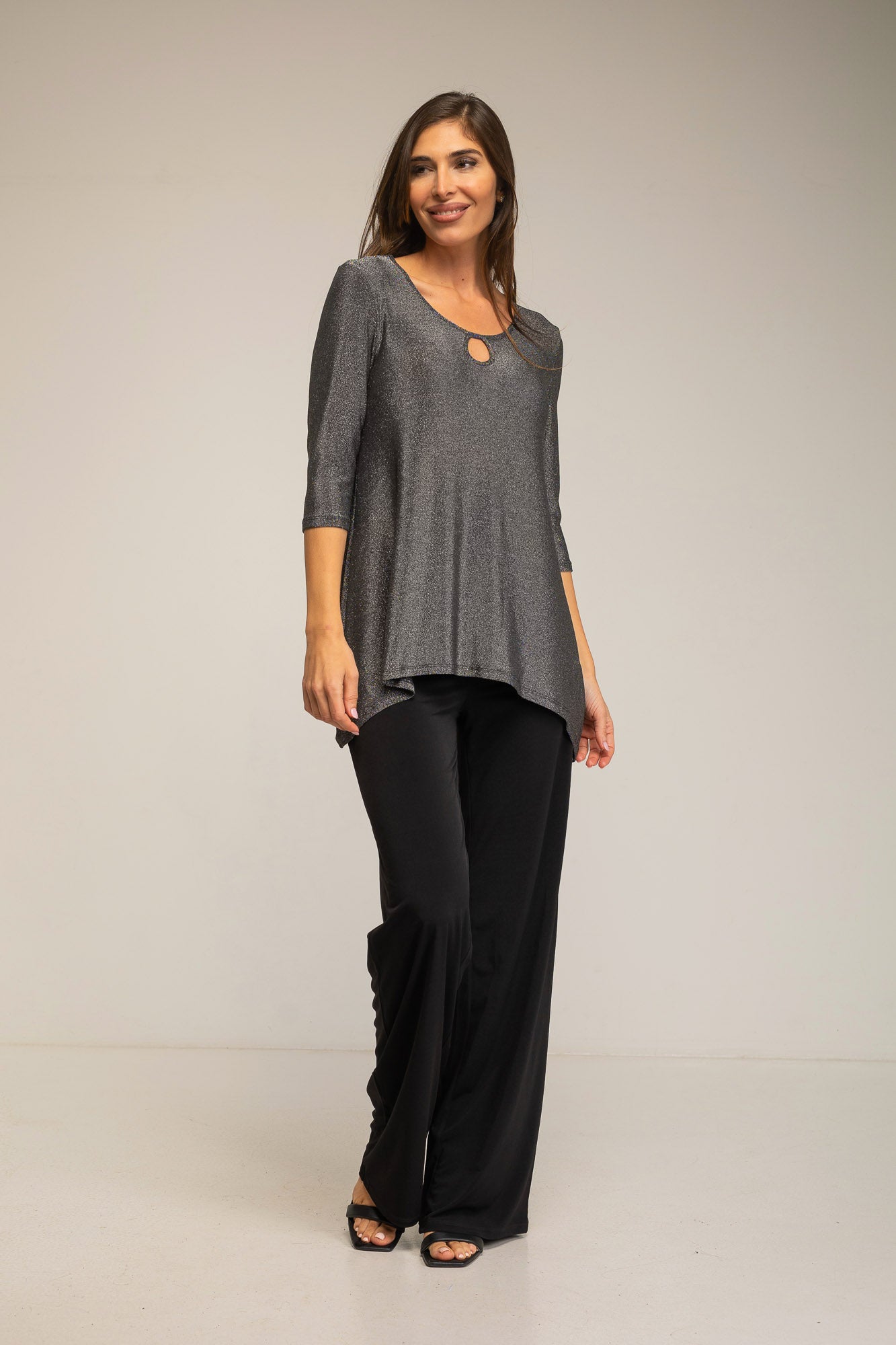 Woman wearing a gray top and black pants on a plain background