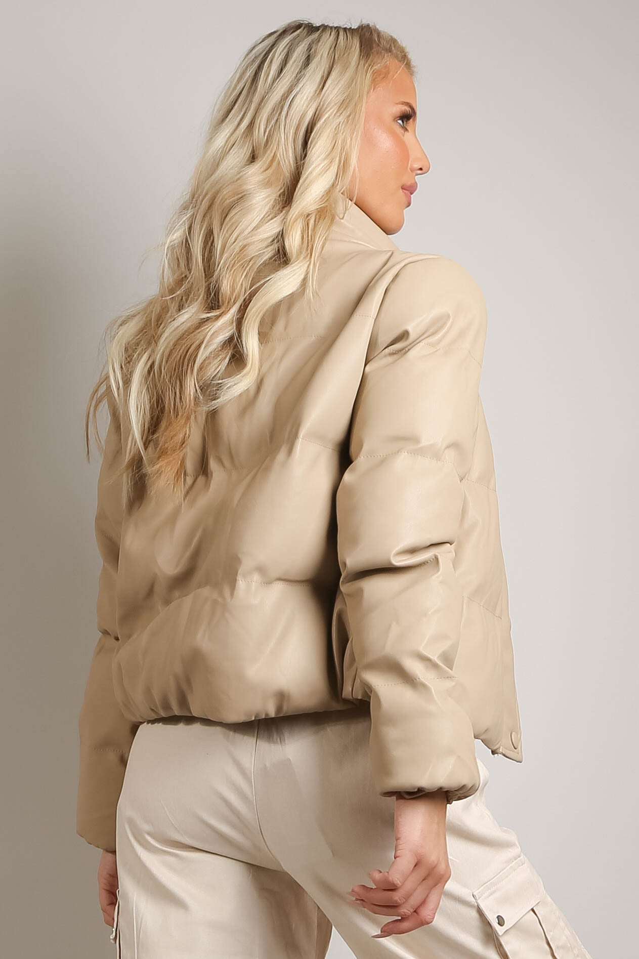 Woman wearing a beige puffer jacket and pants against a plain background