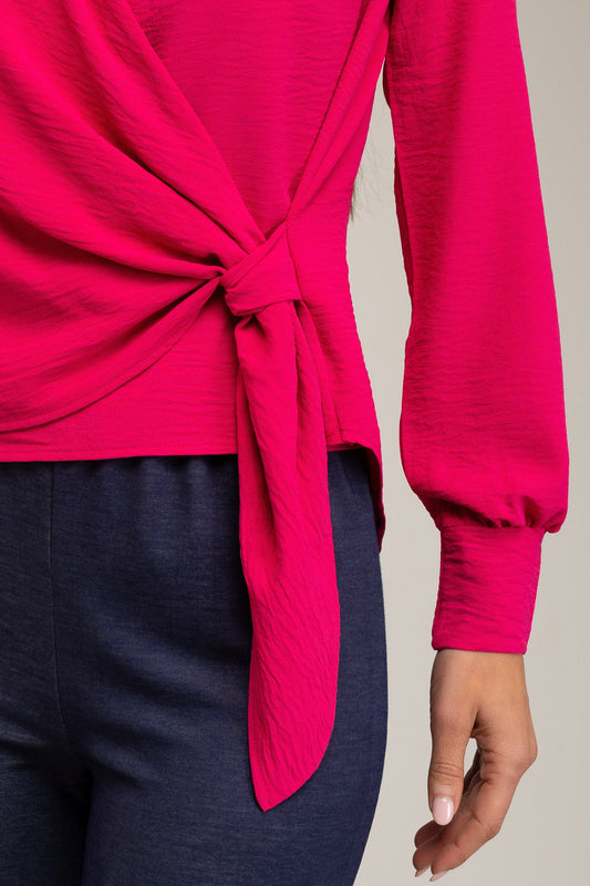 Close-up of a bright pink top with a knot detail worn by a person, on a neutral background.