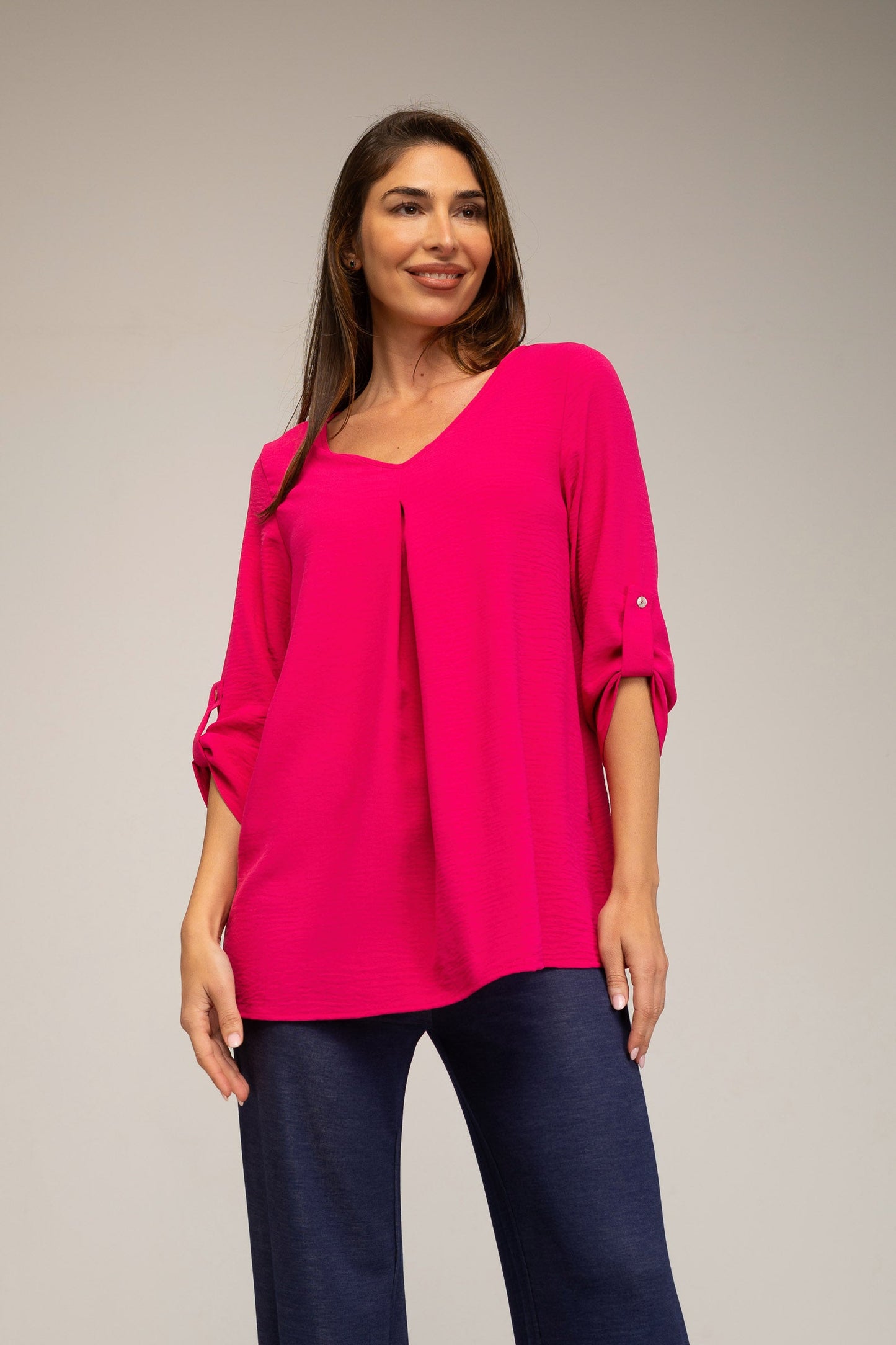 Woman wearing a bright pink top and dark blue pants on a plain background