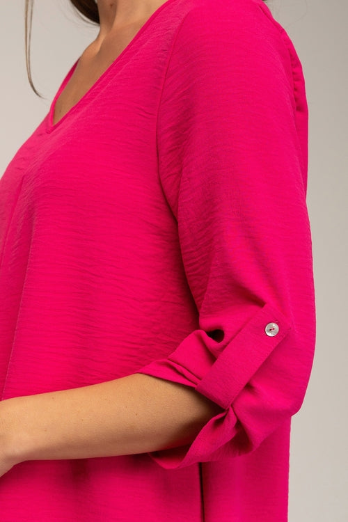 Close-up of a bright pink blouse with rolled-up sleeves on a neutral background