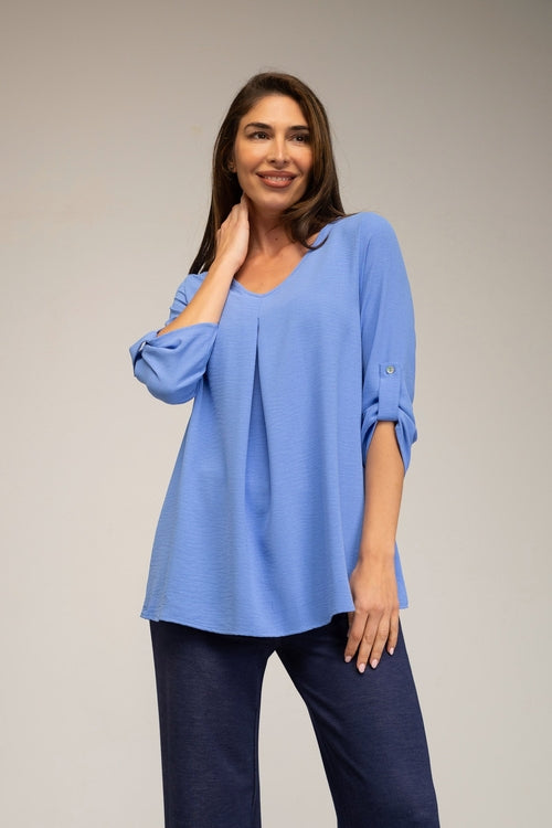 Woman wearing a light blue blouse with rolled-up sleeves against a plain background