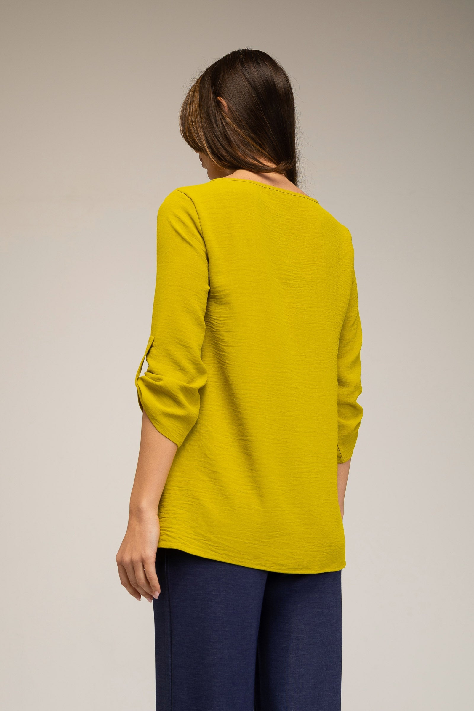 Person wearing a yellow long-sleeve top and blue pants on a plain background