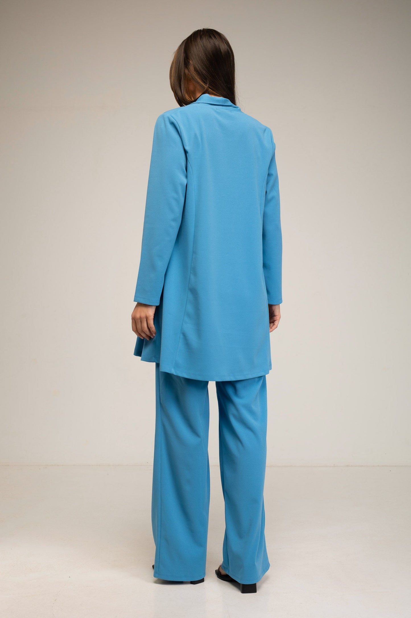 Person wearing a blue suit standing against a plain background