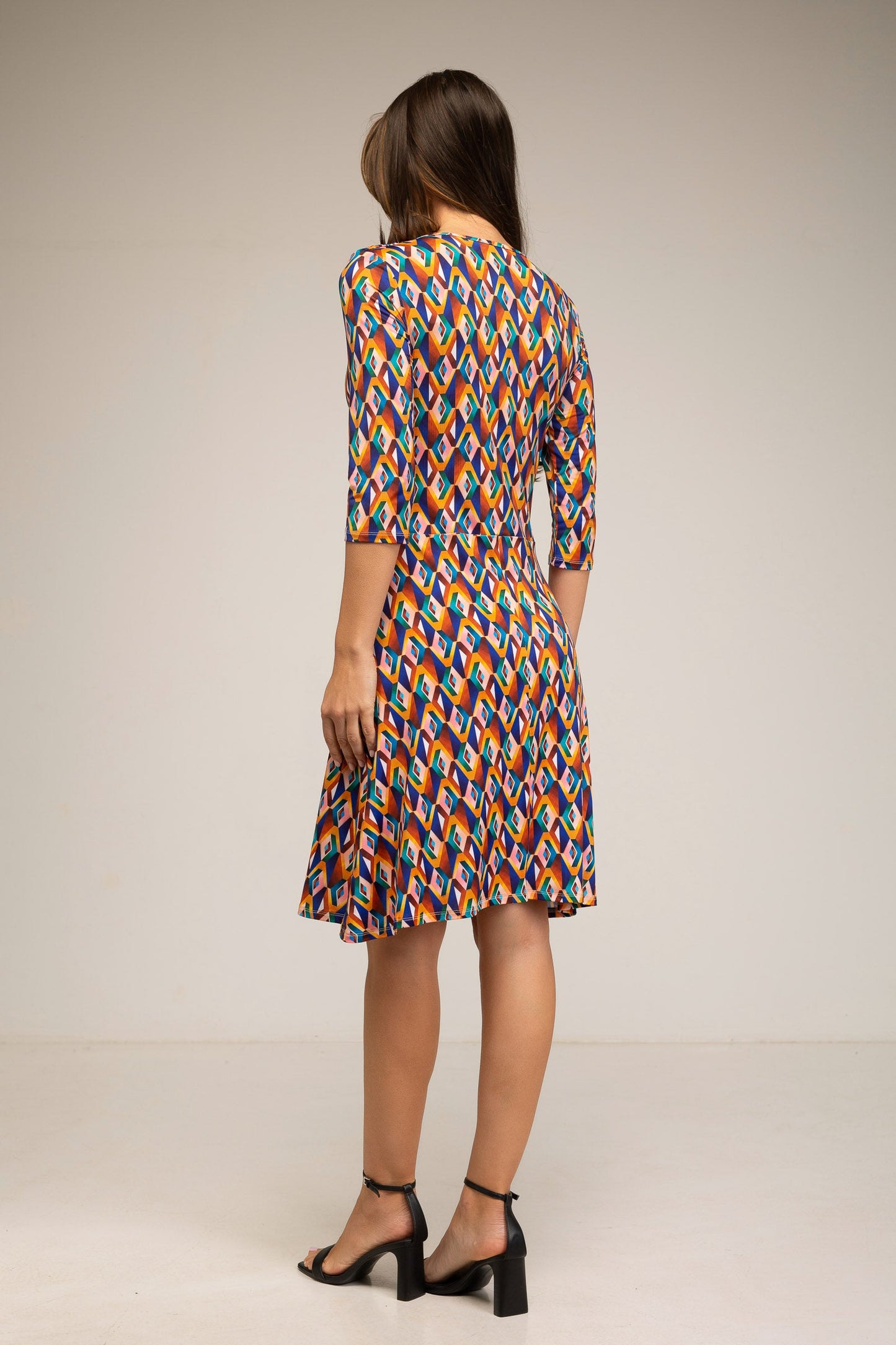 Woman wearing a colorful geometric patterned dress on a plain background