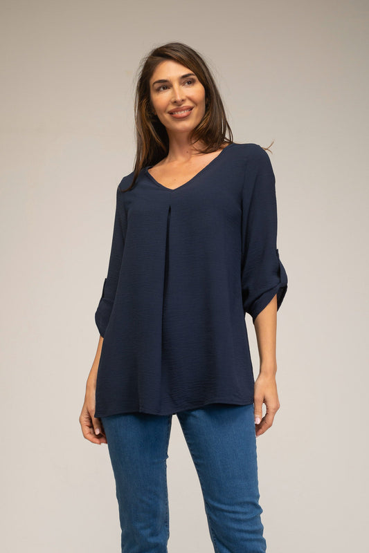 Woman wearing a navy blue top and blue jeans against a plain background