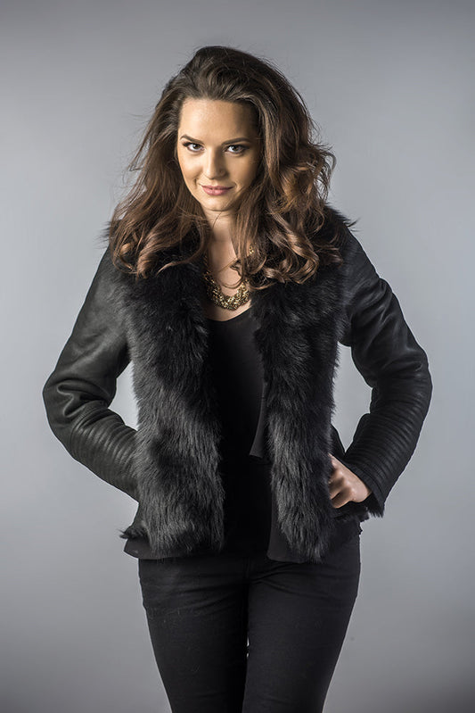 Woman wearing a black leather jacket with fur trim against a gray background