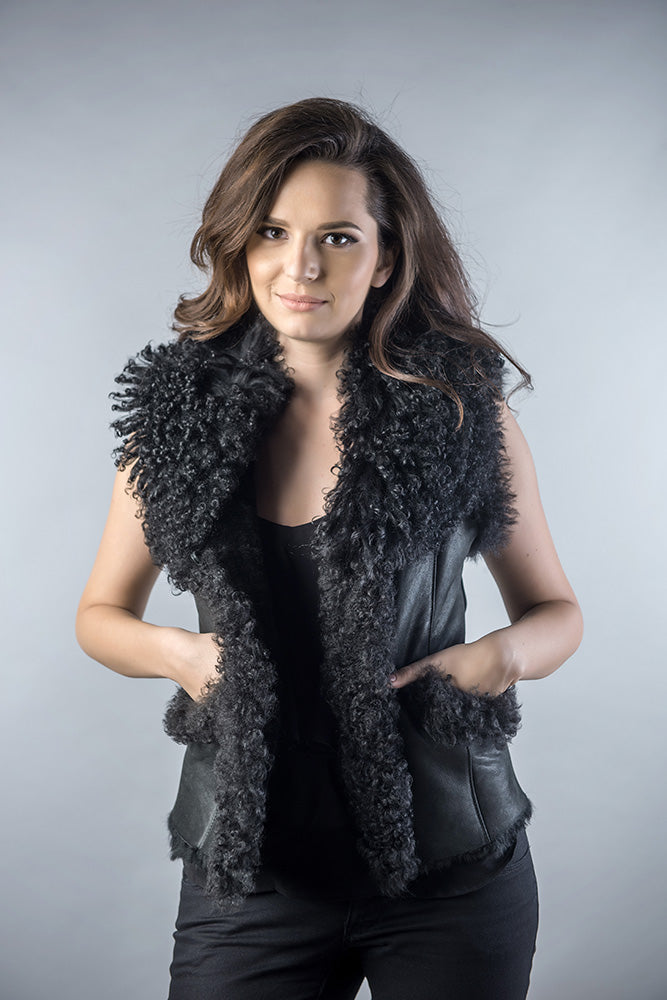 Woman wearing a black fur vest over a black top against a gray background