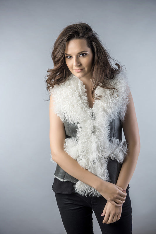 Woman wearing a white ruffled vest over a gray top against a plain background