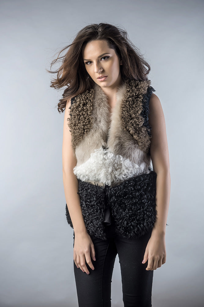 Woman wearing a layered outfit with a fur vest and black pants on a plain background