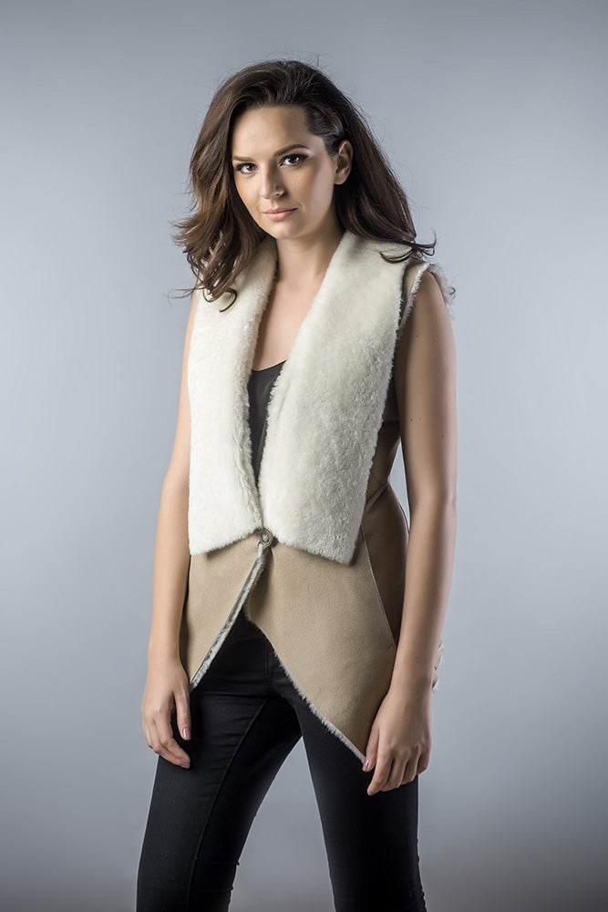 Woman wearing a beige and white shearling vest against a gray background