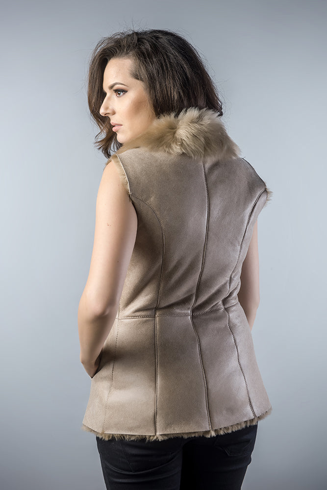 Woman wearing a beige suede vest with fur collar on a gray background