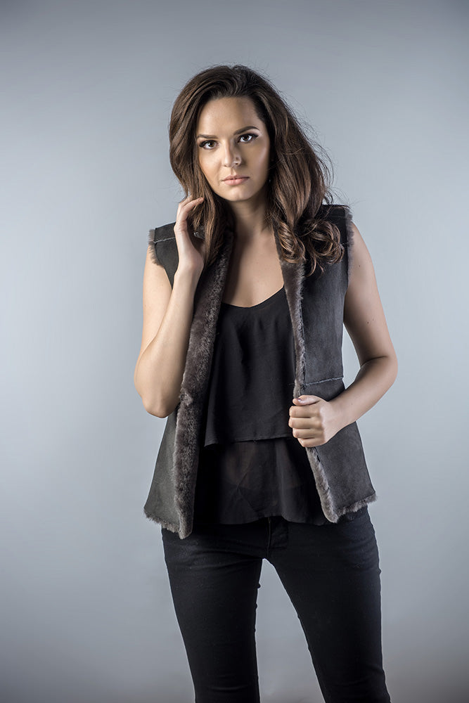 Woman wearing a dark gray vest over a black top and pants on a gray background