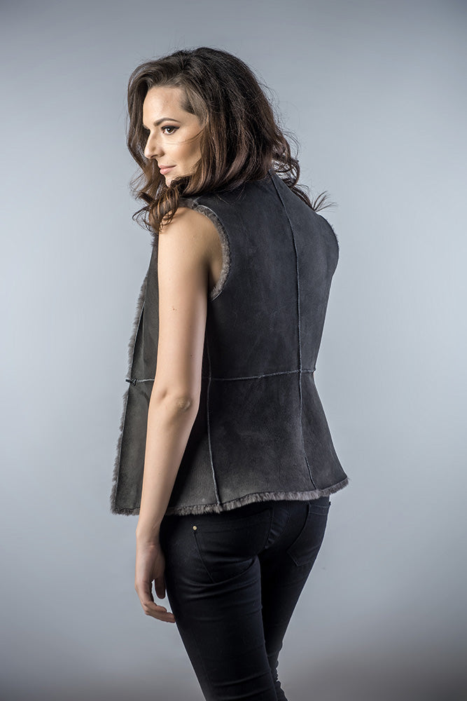 Woman wearing a dark gray sleeveless jacket against a plain background