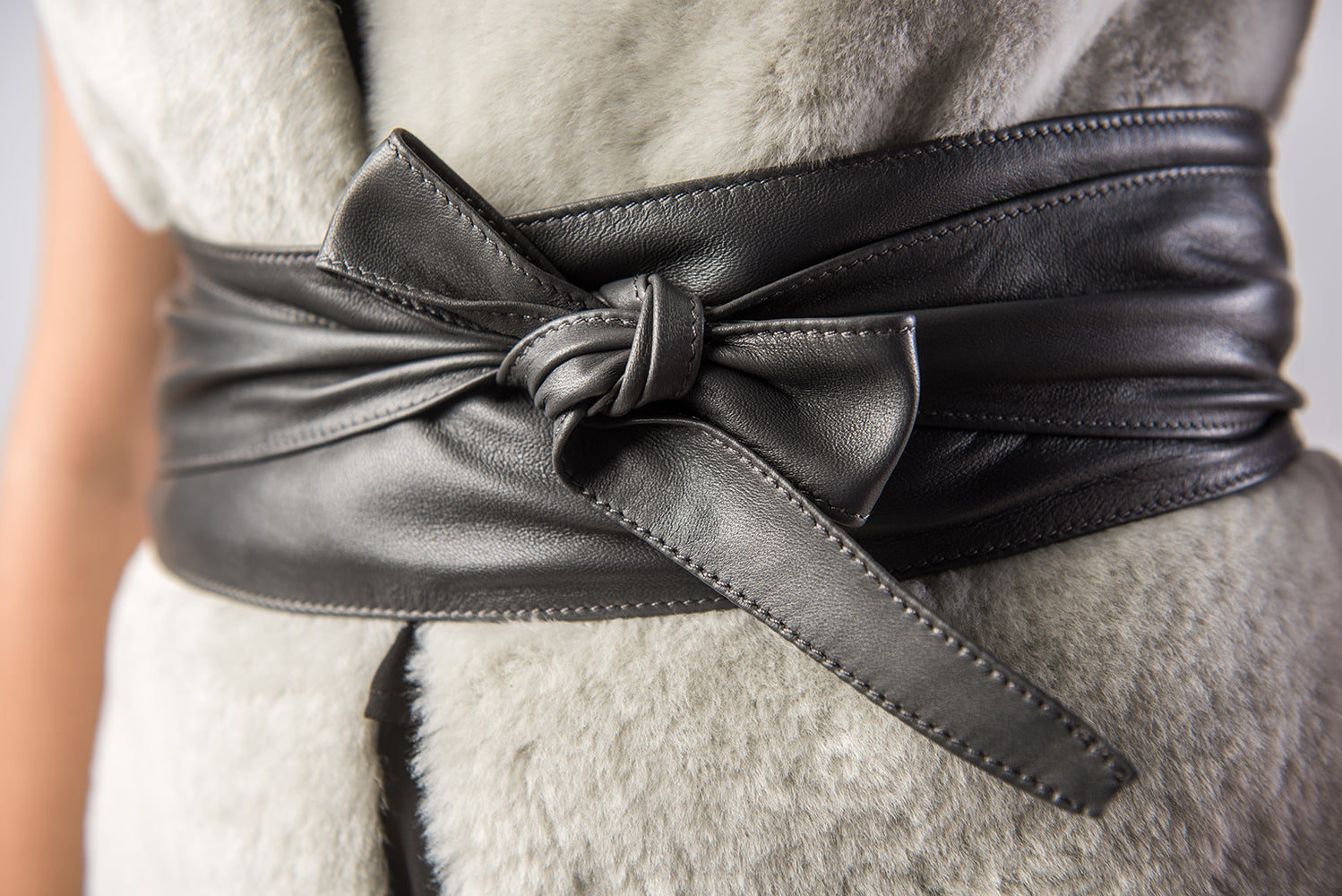 Black leather belt with a large bow worn by a person in a light-colored outfit.