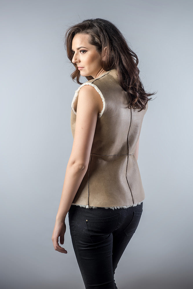 Woman wearing a beige vest over a black top on a gray background